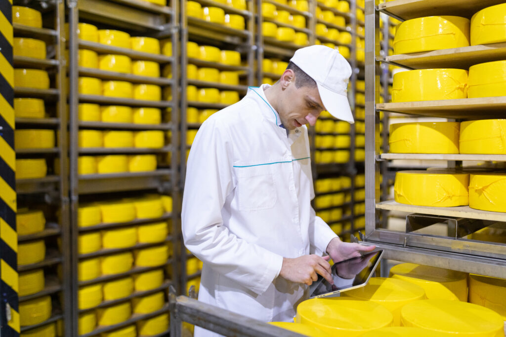 technologist white robe holding tablet records stands near shelves with cheeses production cheese products man cheese shop